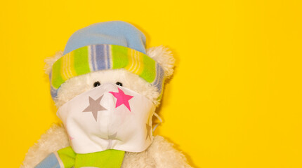 big teddy bear sitting in a mask on a yellow background, the concept of protection against respiratory diseases, viruses and personal respiratory protection
