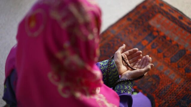 Closeup of a muslim woman hands while praying with prayer beads on prayer rug.