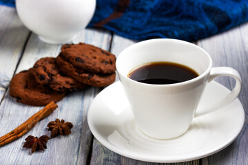 A cup of coffee, cookies with chocolate chips and cinnamon sticks on a white table. Morning coffee at the coffee shop.
