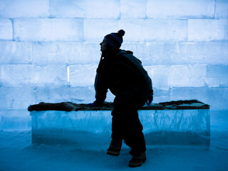 Silhouette of a girl with cap and snow overalls inside an ice igloo - obrazy, fototapety, plakaty
