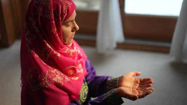 Mature Muslim woman praying at home with beautiful light with snow on the ground. Concept of female prayer in home environment.