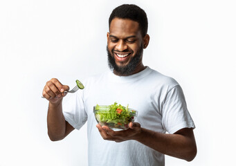 Happy Black Man Eats Fresh Vegetable Salad Over White Background