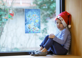 Ein kleiner Junge sitzt mit Weihnachtsmütze am Fenster