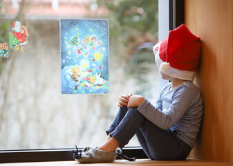 Ein kleiner Junge sitzt mit Weihnachtsmütze am Fenster