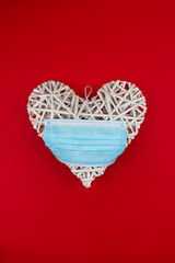 White heart with a blue face mask on a red background. Concept of a Valentine´s day during Coronavirus or Covid pandemic.