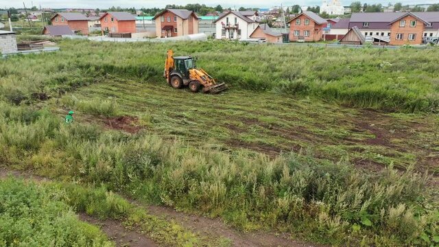 Excavator clears grass on land. Clip. Bulldozer clears grass on land plot. Bulldozer prepares plot of land for construction of country house