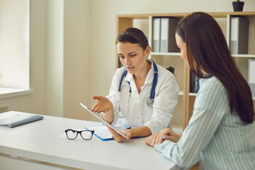 Woman doctor therapist communicating with patient and showing her research results during visit in medical clinic