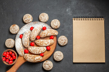 Top view of tasty cookies on and round the cutting board with red cornel berries and notebook
