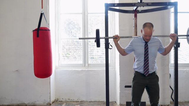 Man in a suit doing squats. Businessman doing exercises with barbell in the gym. a successful business, revenue growth, and reaching goals concept. Businessman with a barbell in heavy lifting.