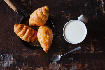 Breakfast bread, croissants and fresh milk on the wooden table.