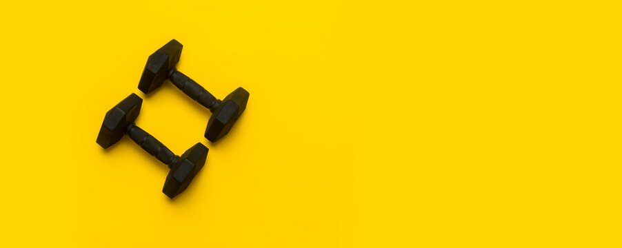 Black dumbbell on yellow background. Top view, space for your text.