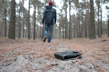 Young man loses his purse with euro money bills on Russian autumn fir wood path. Carelessness and...