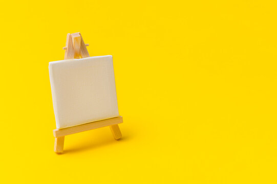 Wooden molbert with a paper attached to it isolated on a yellow background