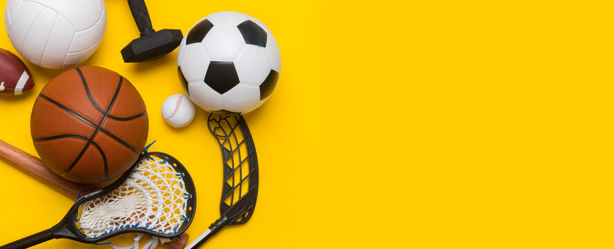Assorted sports equipment including a soccer ball, volleyball, baseball, american football, lacrosse and hockey on a blue background. Top view, space for your text