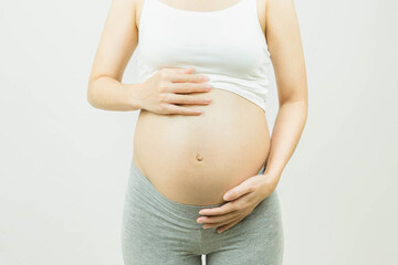 pregnant woman caressing her belly over gray background-Motherhood, pregnancy, people and expectation concept.