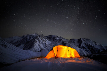 Glowing orange tent in the night winter mountains