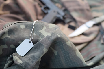 Army Dog tag token with Knife and pistol lie on folded camouflage green fabric