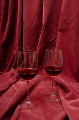 Vertical image.Two glasses and red wine in it, pink decorative textile