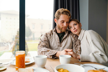 Beautiful romantic young couple hugging while having breakfast at home