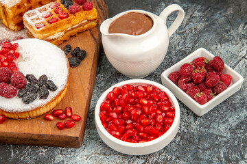bottom close view different berry cakes on cutting board bowls of raspberries pomegranates liquid chocolate on grey-white background