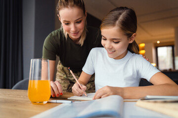 Beautiful happy military woman doing homework with her daughter at home