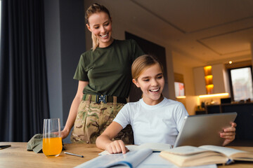 Beautiful happy military woman doing homework with her daughter at home