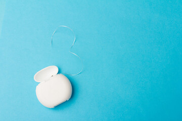 Dental floss container on blue background. Daily oral hygiene, teeth care and health. Cleaning products for your mouth, copy space. Dental care concept.