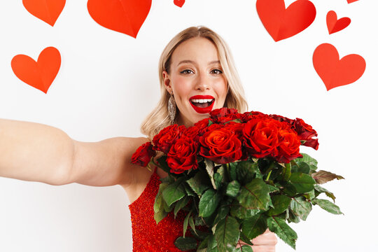 Happy nice girl in red dress holding roses and taking selfie photo