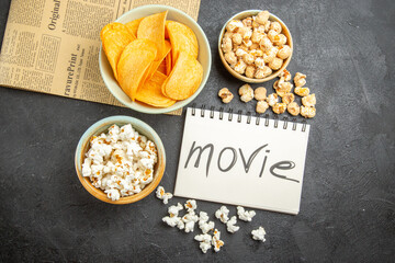 top view tasty cheese cips with different snacks and movie written notepad on dark background cinema photo nut potato food movie