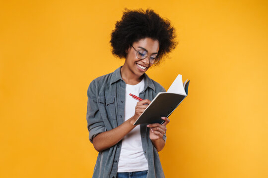 Joyful african american girl in eyeglasses writing in exercise book