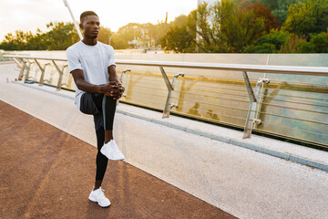 Relaxed african sportsman stretching on the bridge