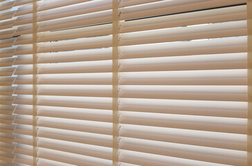 Wood blinds closeup in the interior. Automatic venetian blinds beige color on large windows. Coulisse wooden slats 50mm wide. Wood floor, beige walls.