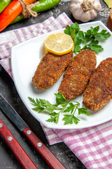 bottom close view cutlets lemon slice parsley on white plate fork and knife red pepper kitchen towel on grey background