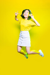 Fototapeta na wymiar Young asiatic woman jumping on yellow background listening music - Excited youthful energetic asian woman enjoying music isolated