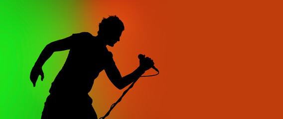 Fototapeta na wymiar Flyer. Silhouette of young male guitarist isolated on green-orange gradient studio background in neon. Beautiful shadow in action, performing. Concept of human emotions, expression, ad, music, art.