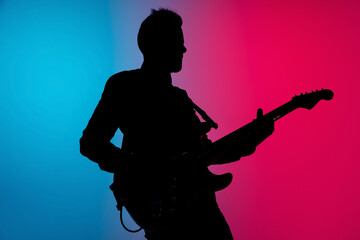 Dancing. Silhouette of young male guitarist isolated on blue-pink gradient studio background in neon. Beautiful shadow in action, performing. Concept of human emotions, expression, ad, music, art.