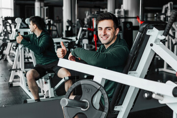 Fototapeta na wymiar The young coach in the gym, looks at the camera with a smile and shows okay