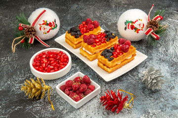 bottom view berry waffles on white rectangular plate bowls of pomegranate and raspberries and white xmas tree balls on grey-white background