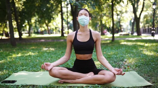 Athletic young woman in a medical protective mask, doing yoga in the Park