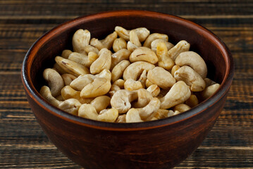 Cashews in a clay bowl on an old shabby board. Nuts on a brown wooden table.
