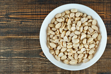 Peanuts in a white bowl on an old shabby board. Nuts on a brown wooden table.