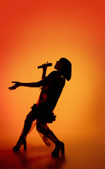 Dance. Silhouette of young female singer isolated on orange gradient studio background in neon light. Beautiful shadow in action, performing. Concept of human emotions, expression, ad, music, art.