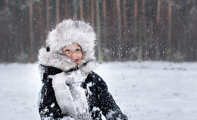 Happy child in winter clothes rejoices in the snow and laughs
