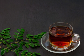 moringa tea in glass cup and moringa leaf on black wooden background