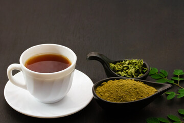 moringa tea in white cup ceramic powder in black bowl and moringa leaf on black wooden background