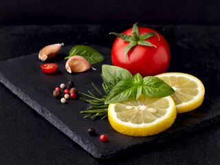 Fresh tomato with basil leaves, rosemary, lemon and pepper  isolated on black background.