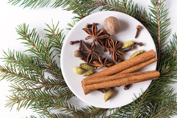 spices for mulled wine on a small white plate on a white background with green branches of a Christmas tree. the view from the top