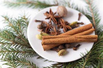 Obraz na płótnie Canvas spices for mulled wine on a small white plate on a white background with green branches of a Christmas tree. the view from the top