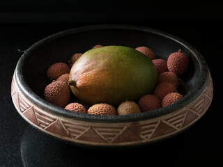 Fototapeta na wymiar A mango surrounded by lychees in a bowl with black background