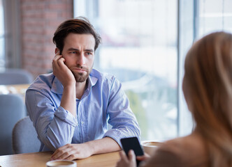 Gadget overuse concept. Bored young guy having dull date, his girlfriend stuck in smartphone at...